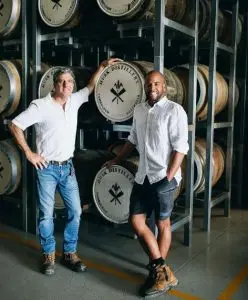 Two men standing in front of stacked Ink Distillery barrels