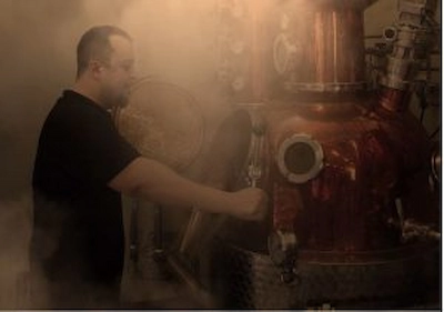 J.Rose Gin distiller operating a traditional copper still in a steamy distillery setting