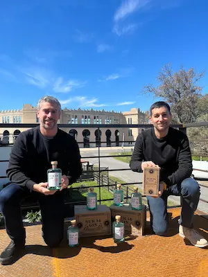 Founders of Sur 34 Gin proudly presenting their craft gin in Uruguay, surrounded by bottles and packaging