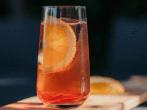 Mediterranean Sunset Sipper cocktail in a tall glass with an orange slice and warm sunset lighting.