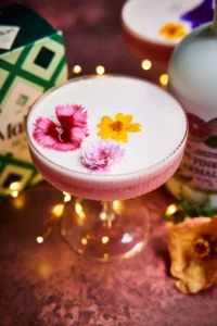 Palma Rose Gin Sour cocktail served in a coupe glass with a floral garnish, featuring a light pink foam layer.