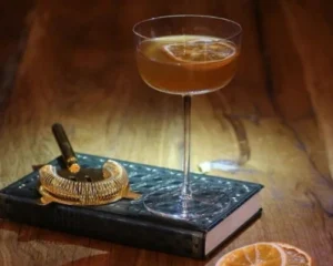 Elegant William of Orange cocktail on a wooden bar with citrus garnish and bar strainer