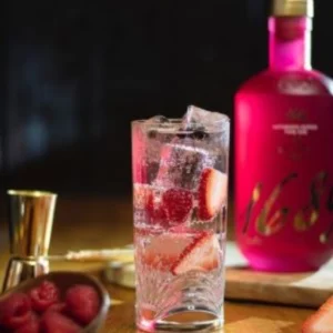 Pink Gin Tonic served with ice and strawberries on a wooden bar