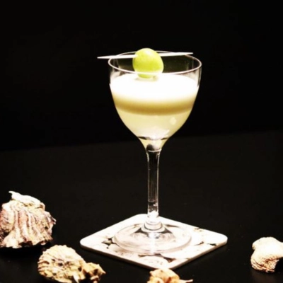 Elegant savoury Gin Sour served in a coupe glass, topped with a green grape garnish against a dark background.