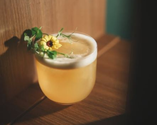 Calamansi gin sour cocktail served in a low glass with floral garnish